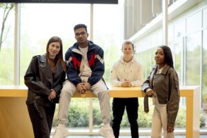 Four students pose around a large yellow desk on the ground floor of the Learning Hub.