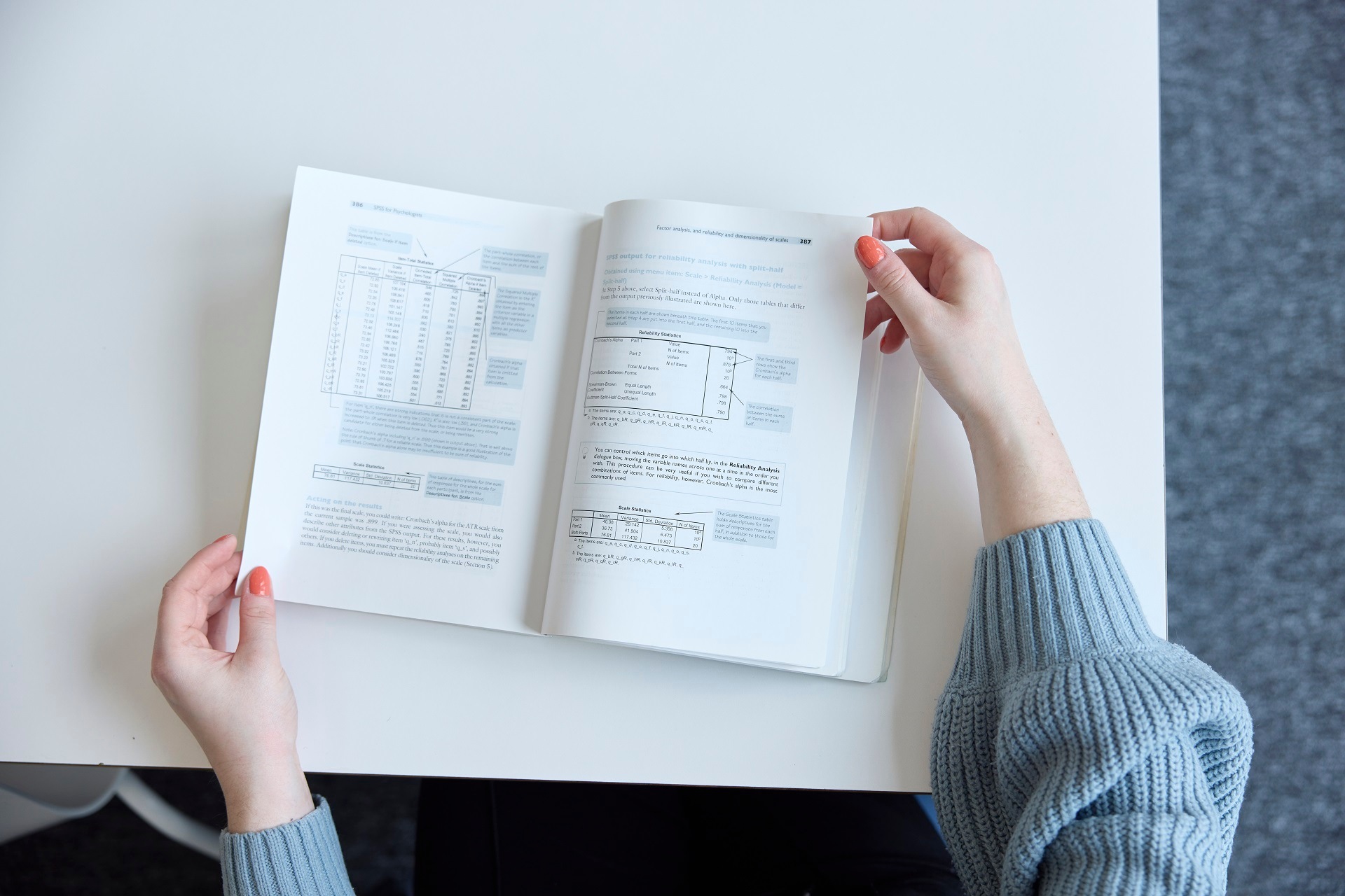 Above view of the hands of a student reading a textbook. She is wearing a light blue jumper and has peach-coloured nails.