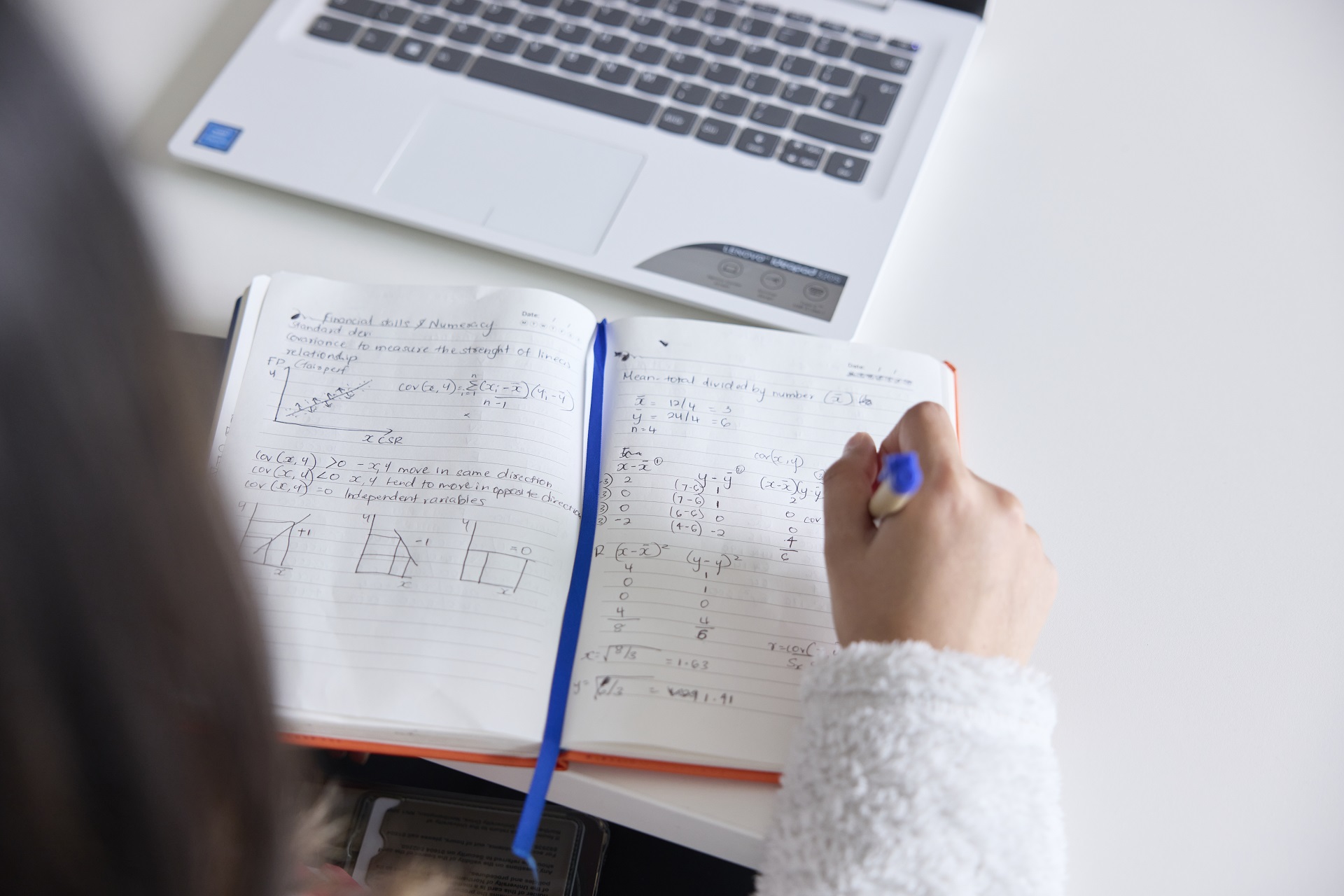 View of student's hand using a pen to take notes of mathematical equations in a notebook