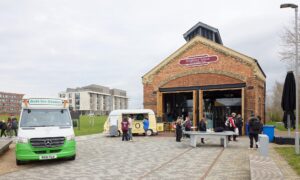 A student union building with a few people gathered outside near an ice cream truck and a small food stand.