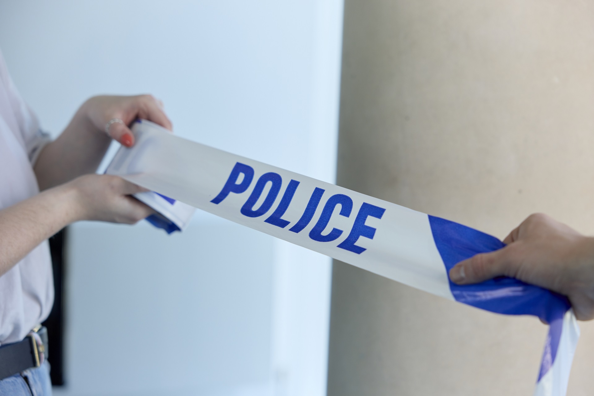 Two students holding blue and white POLICE tape. The neutral background is blurred.