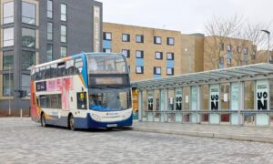 Double-decker bus on a street near a modern building with "UON" signage and a waiting area.