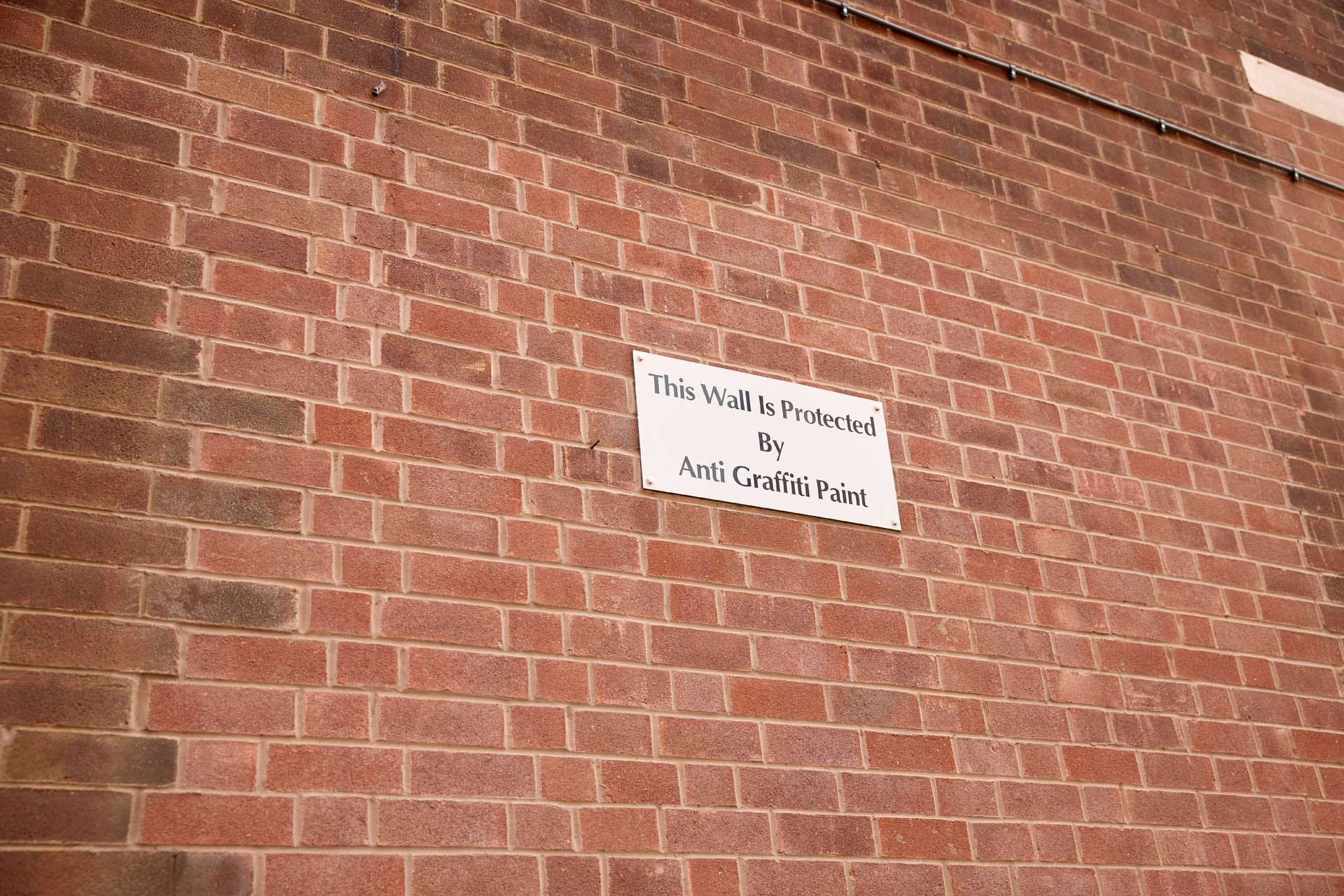 Sign on a brick wall that reads 'This Wall Is Protected By Anti Graffiti Paint'.
