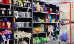 Shelves filled with colourful bags and bins, full of puppets and children's story kits, organized with labelled tags on a library shelf.