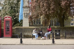 Three female students sat on a bench chatting in Town Centre