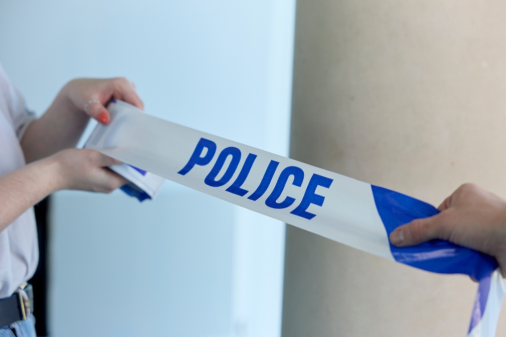 Two people hold a blue and white police tape, stretching it between them indoors near a beige column.