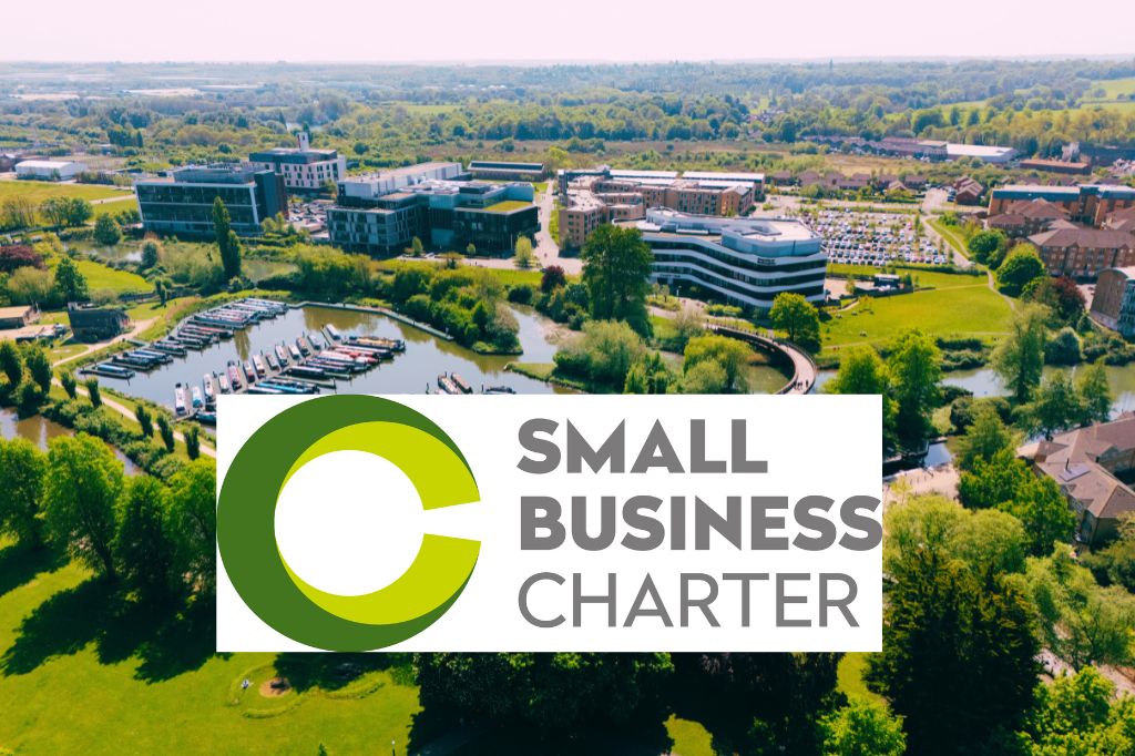 Aerial view of Waterside Campus, home of University of NOrthampton, with a marina, green spaces, and buildings, overlaid with the Small Business Charter logo.