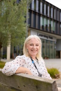 Tracey Russell, Director of Estates & Campus Services sits on a bench outside the Learning Hub building.