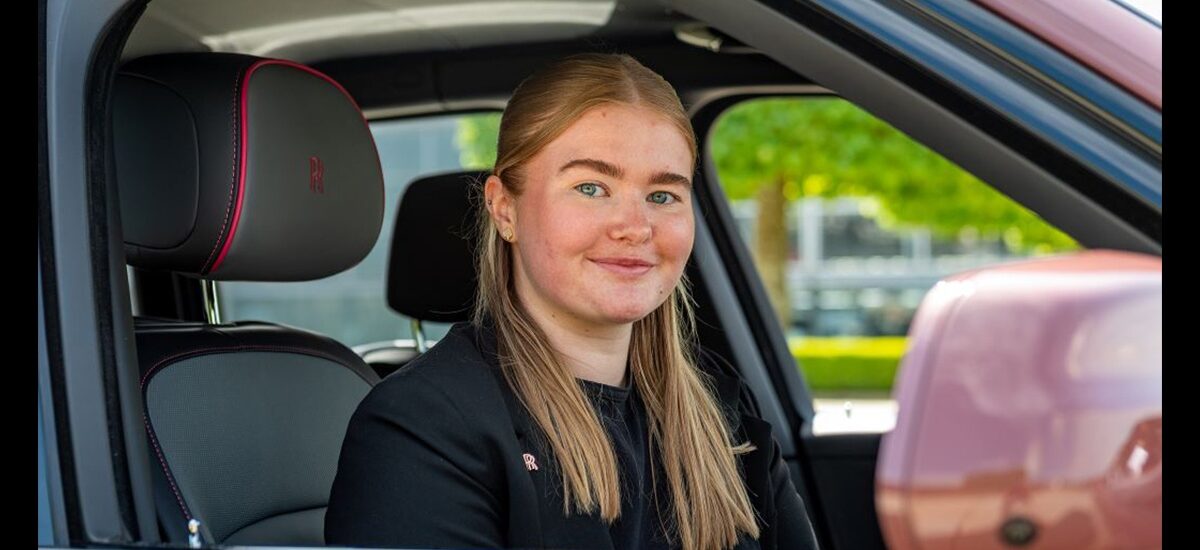 Lydia Roberts, an Advertising and Digital Marketing BA student, sits in the driver's seat of a pink car, looking at the camera with a slight smile.