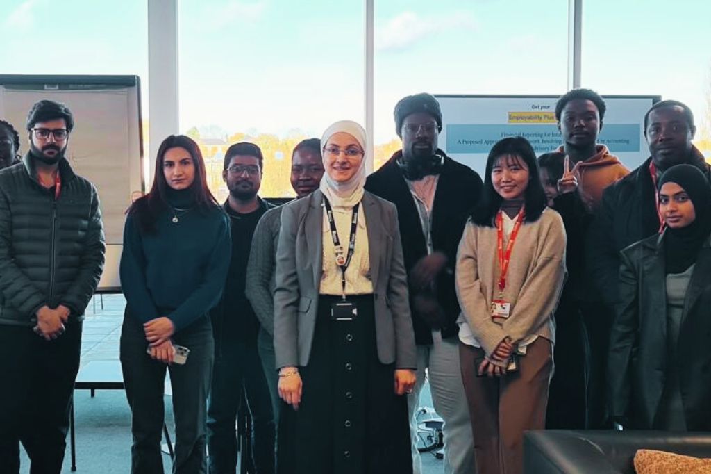 Dr Doaa Aljamal and a group of her students stand in front of large windows and a flip chart, posing for a photo.