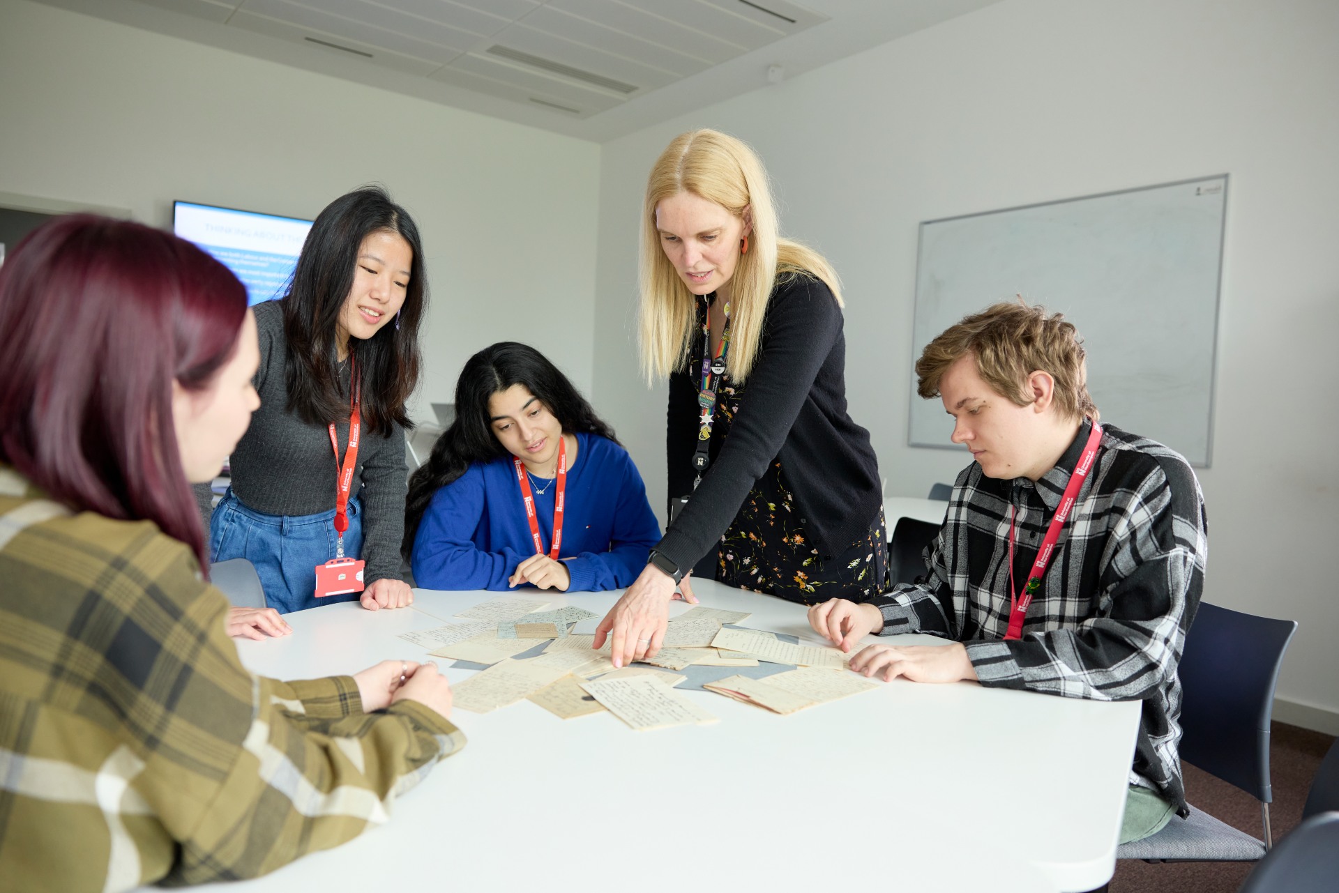 University students collaborating around a table in a classroom setting, actively engaging with printed materials during a group study or workshop session