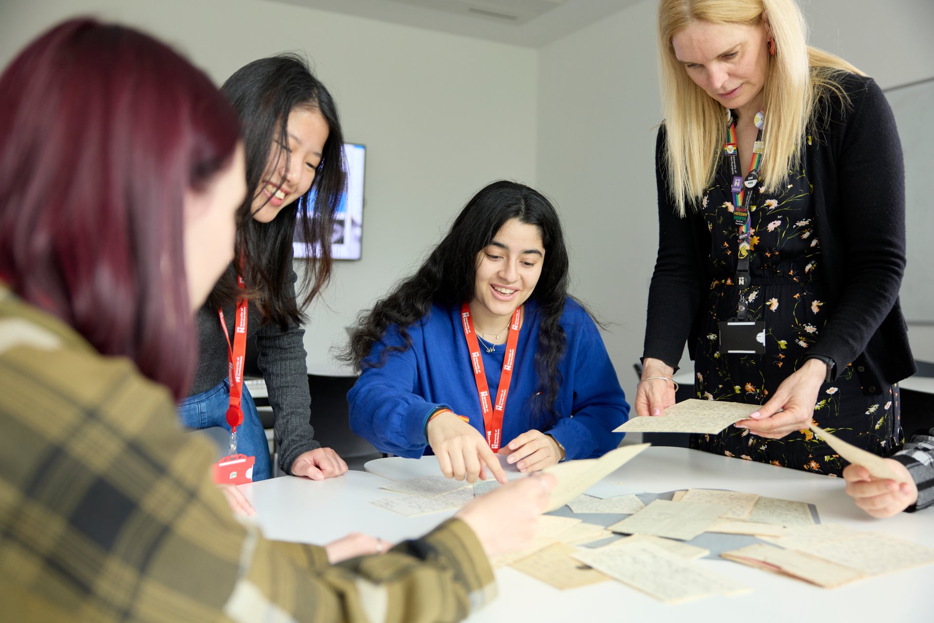 A lecturer works with a small group of students around a table, examining historical documents or handwritten papers during a seminar at the University of Northampton.