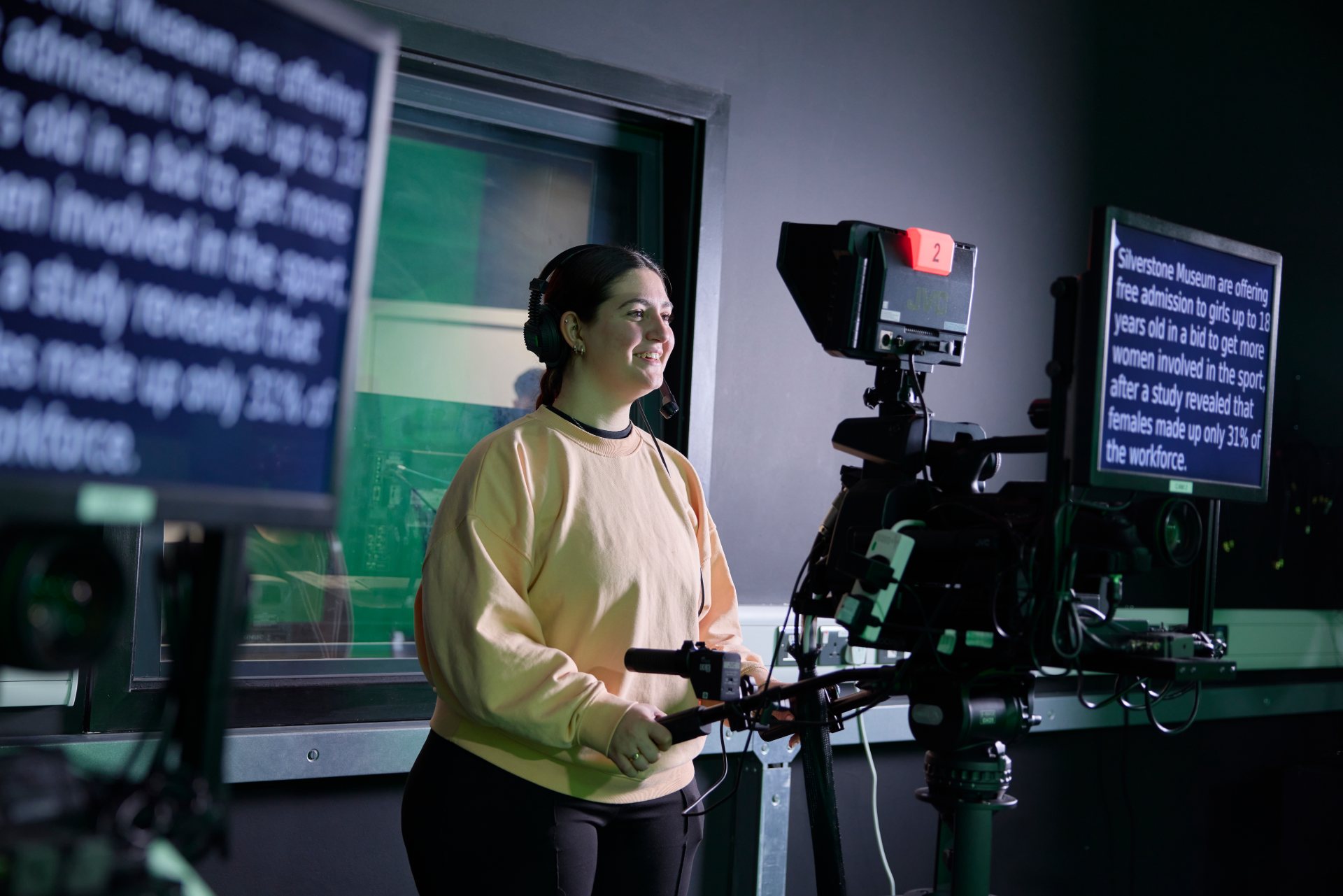 Student operating a professional TV camera with an integrated teleprompter during a journalism studio workshop