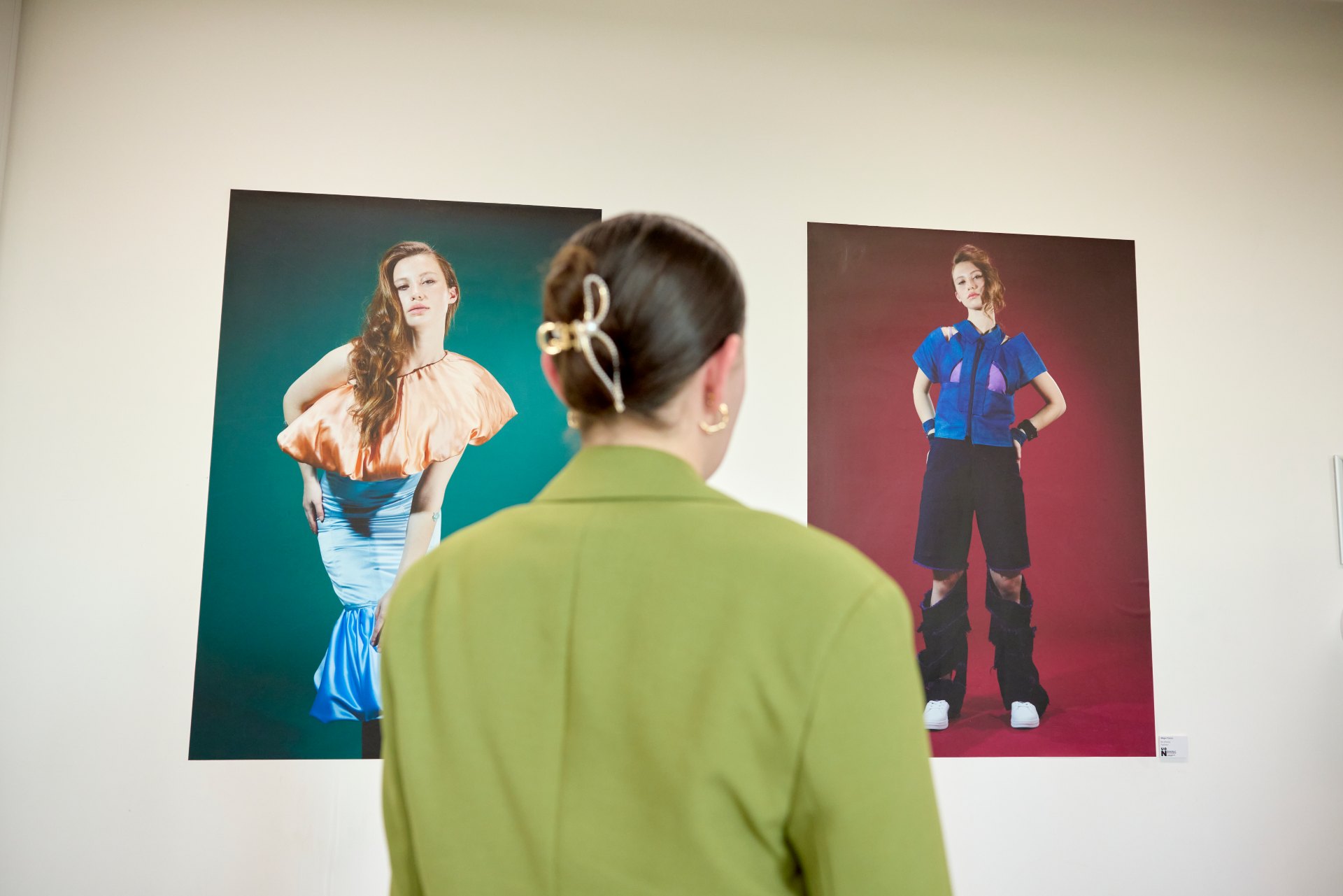 Person viewing two large fashion photography prints displayed on a gallery wall during a university degree show exhibition