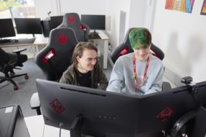 Two Esports students sat side by side in gaming chairs focusing on the two computer screens in front of them.