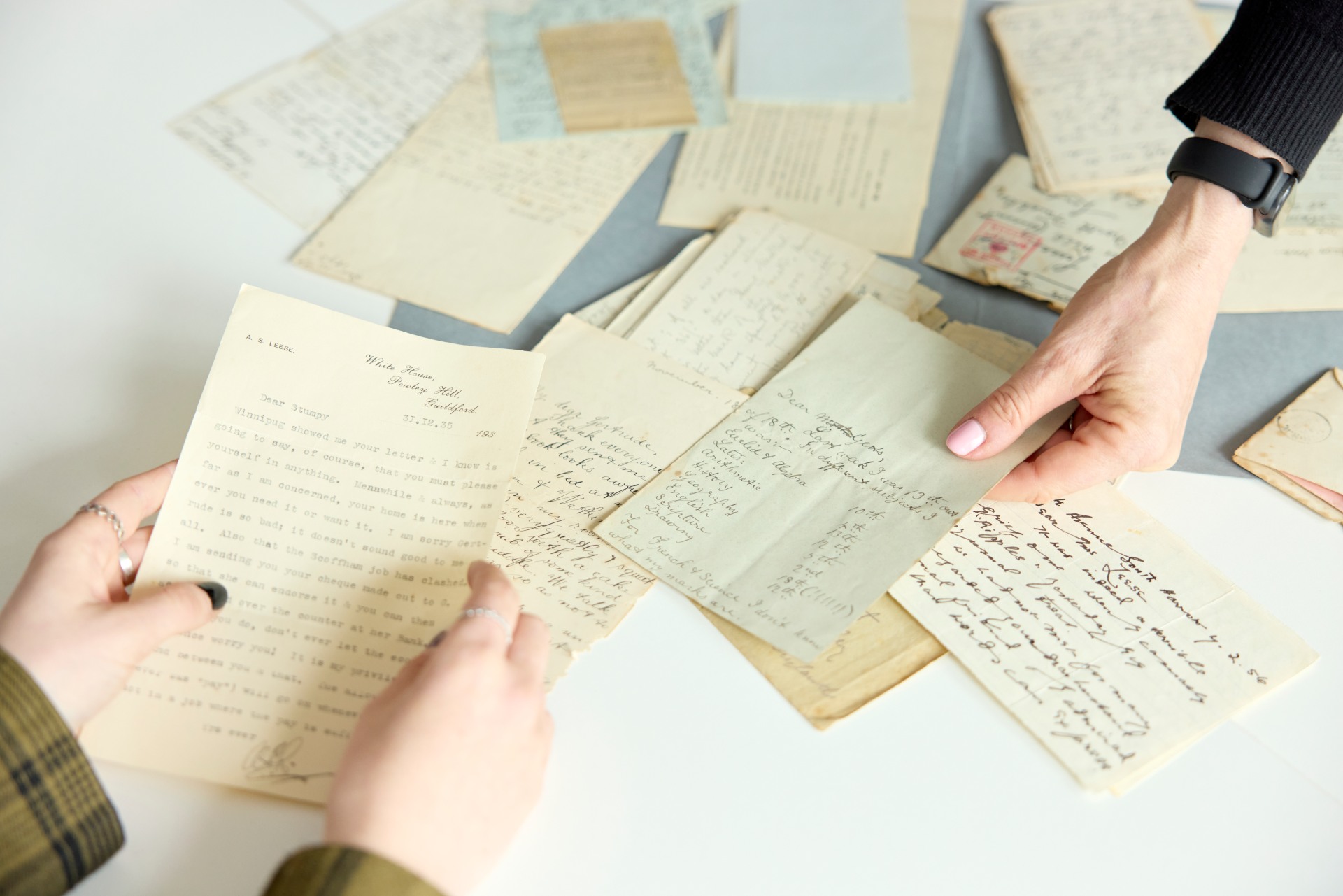 Close-up of two people examining a collection of old handwritten and typed letters spread across a table, as part of a historical or archival study session at the University of Northampton.