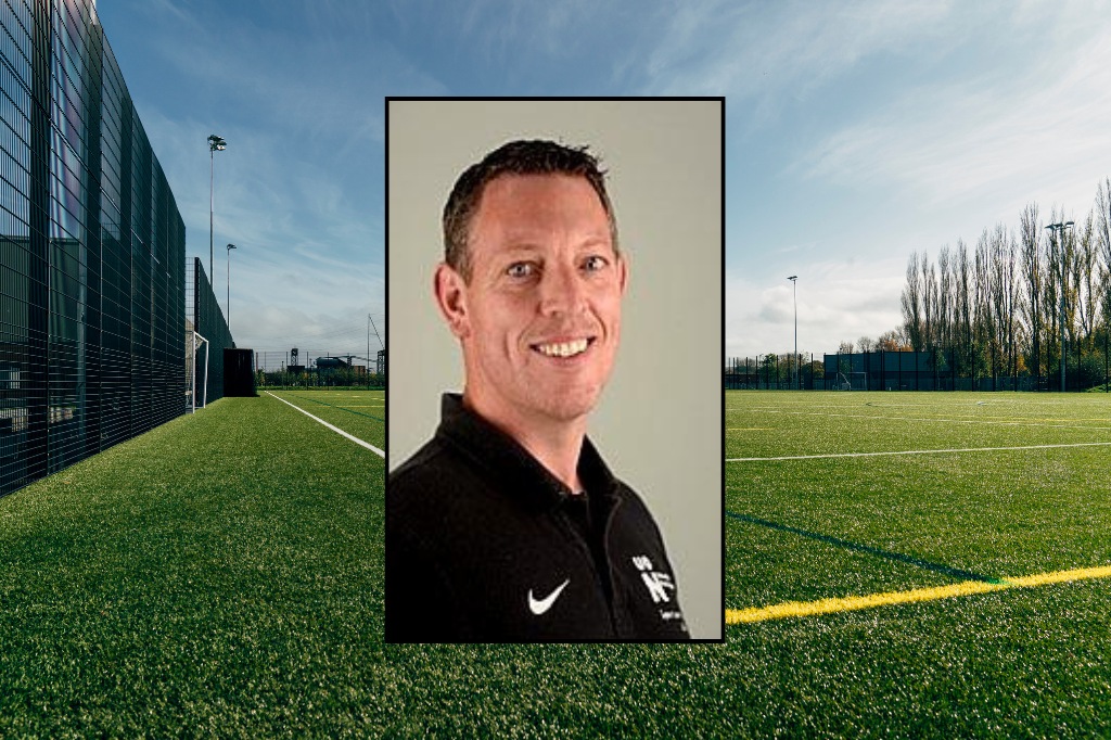A man in a black collared shirt is shown in a portrait photo overlaid on an outdoor sports field with green artificial turf and a blue sky.