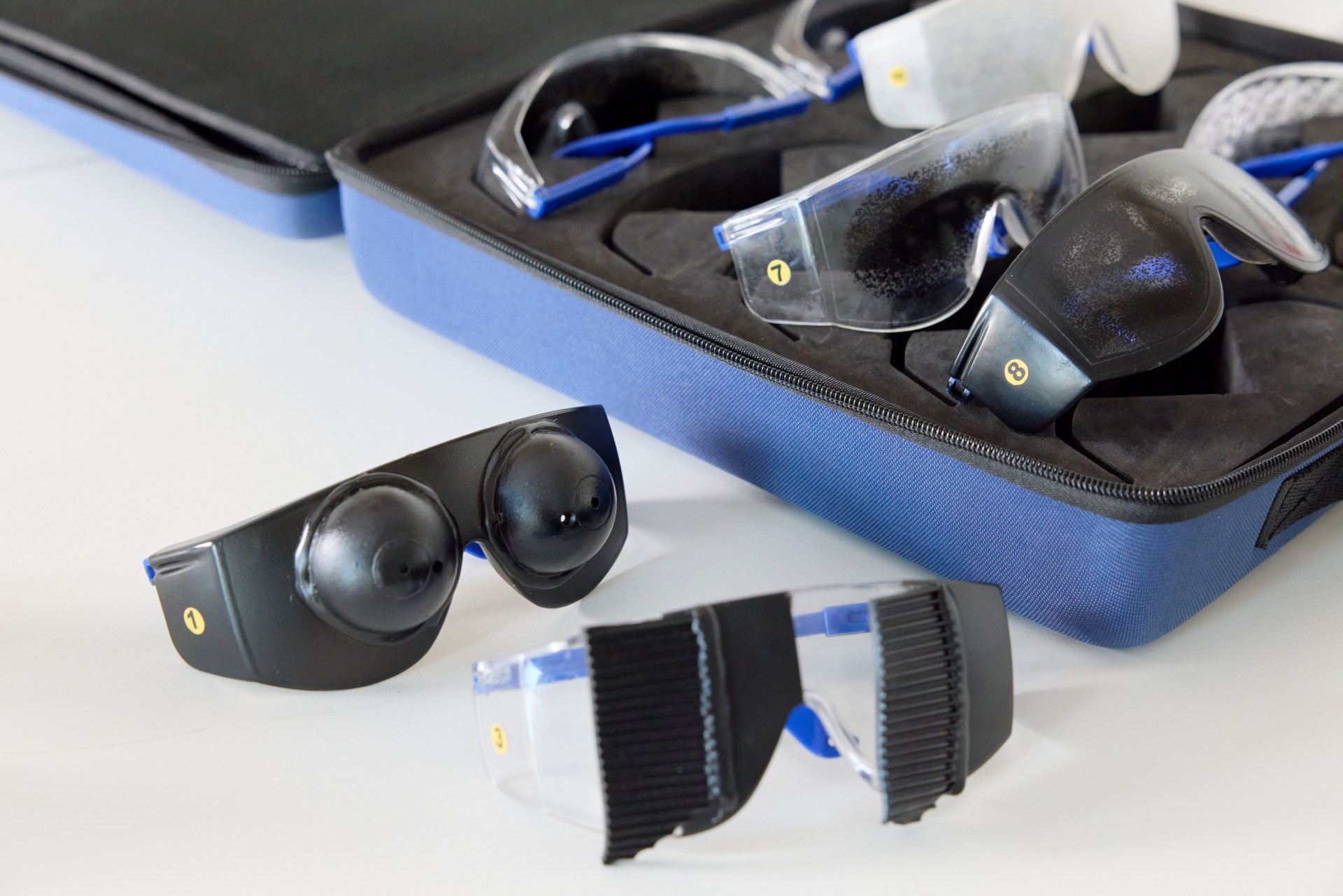 A set of vision impairment simulation glasses and a blue carrying case are displayed on a white surface.