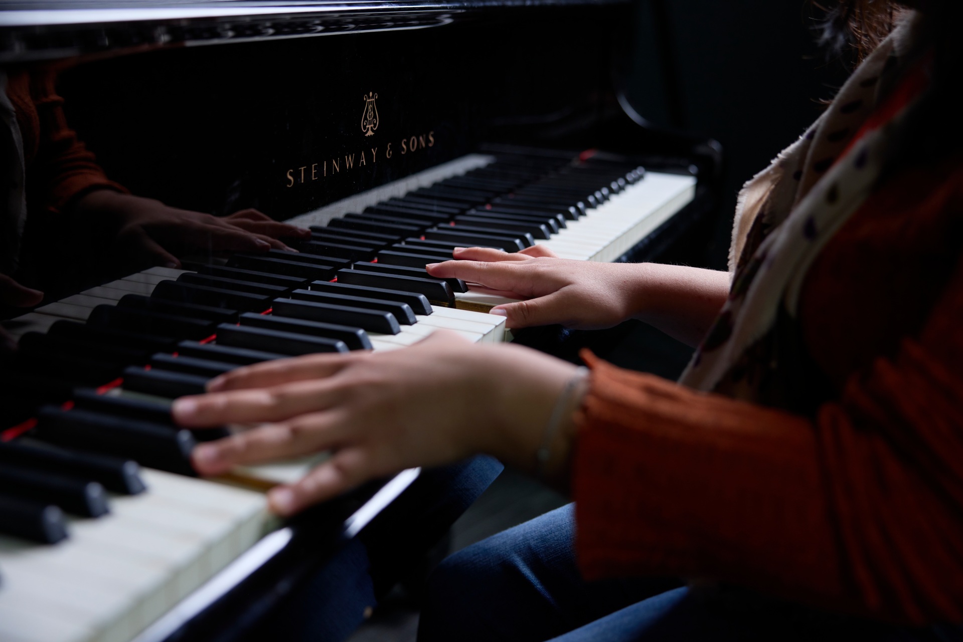 Close-up of a person’s hands playing a Steinway & Sons piano, with the keys and the glossy surface of the instrument in focus.