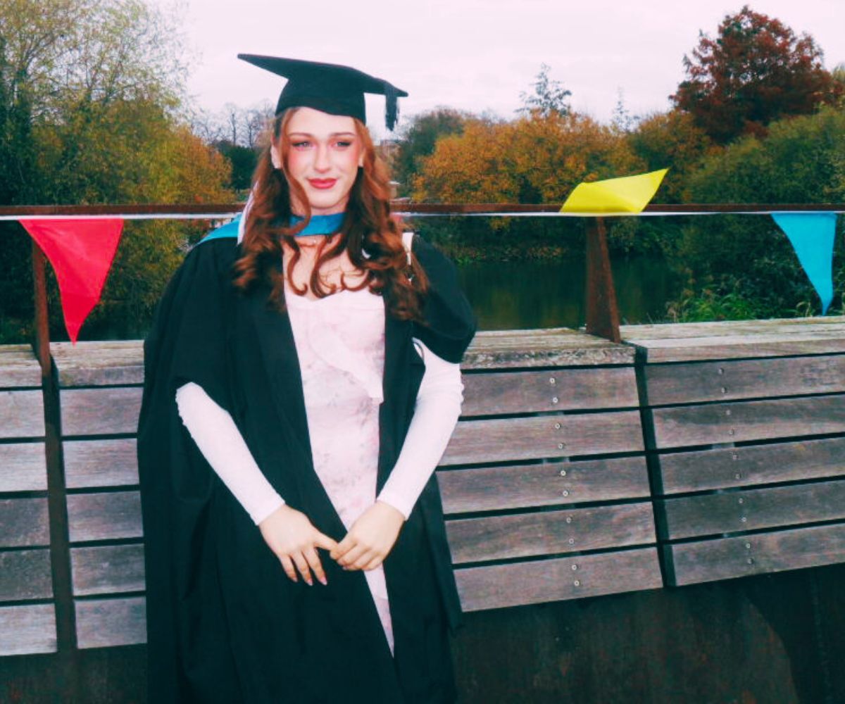 Jayda Franks stands on the footbridge over the River Nene dressed in her graduation gown and mortarboard hat.