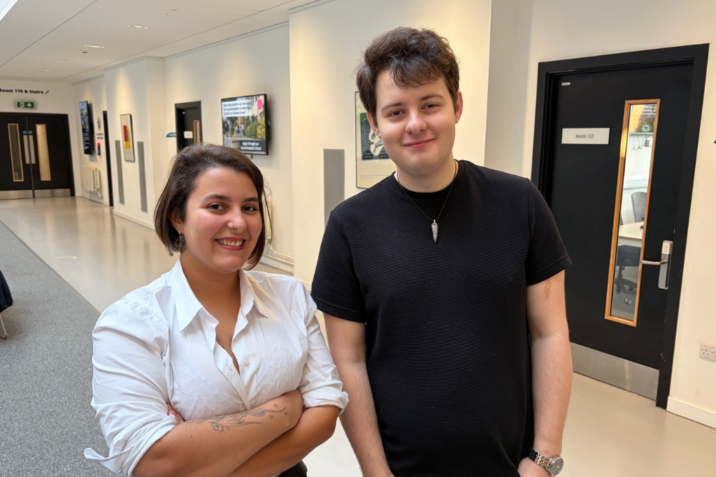 Elisa and Samuel stand beside each other and smile at camera in UON's Creative Hub building.