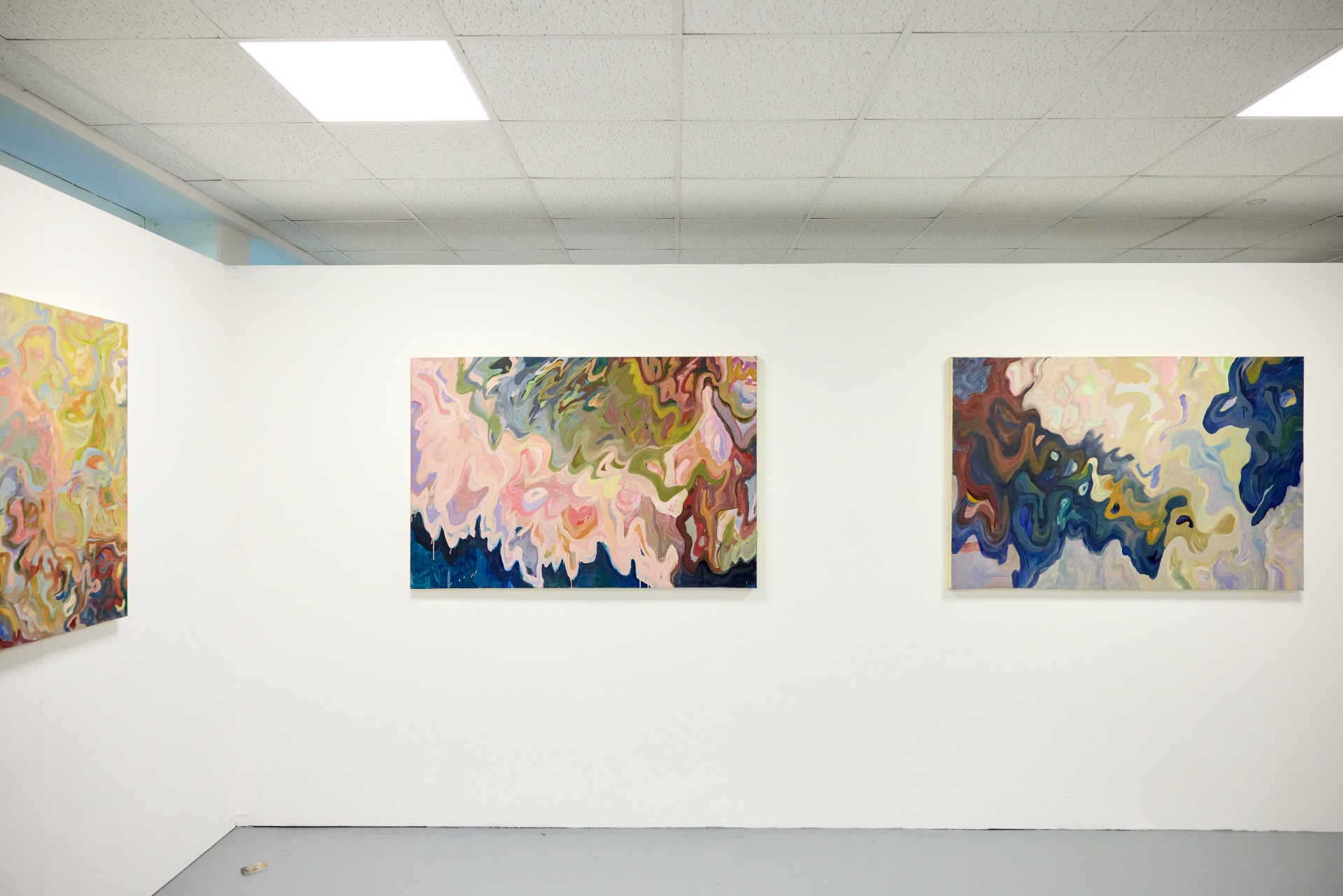 Three colourful abstract student paintings hang on a white gallery wall, featuring flowing, layered shapes in pastel and deep tones.