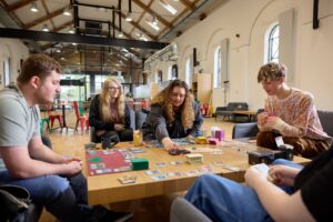 A group of students gathered round a board game rolling dice and playing.