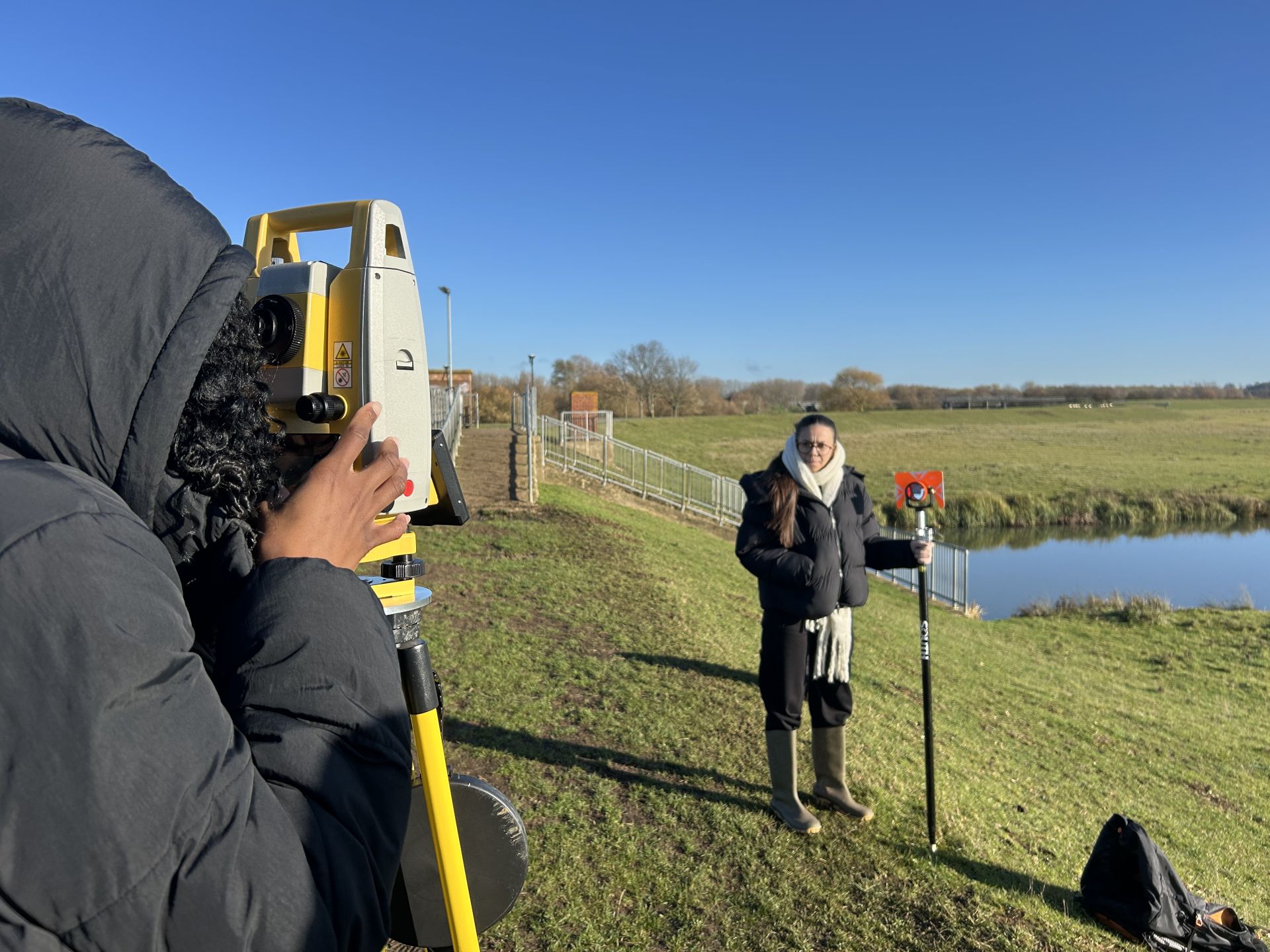 A student looking through a lens whilst another student in a coat opposite holds a long red card.