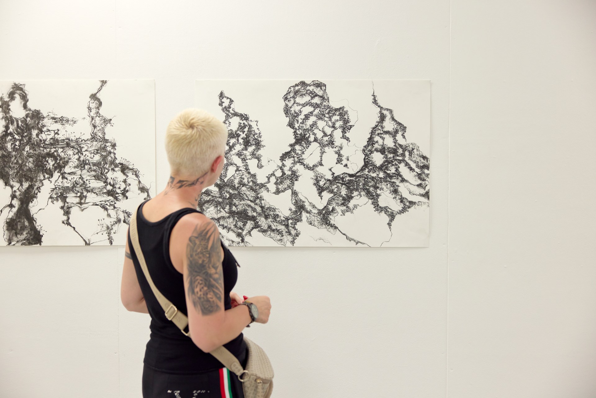 Visitor views two large black-and-white abstract student drawings displayed side by side on a gallery wall.