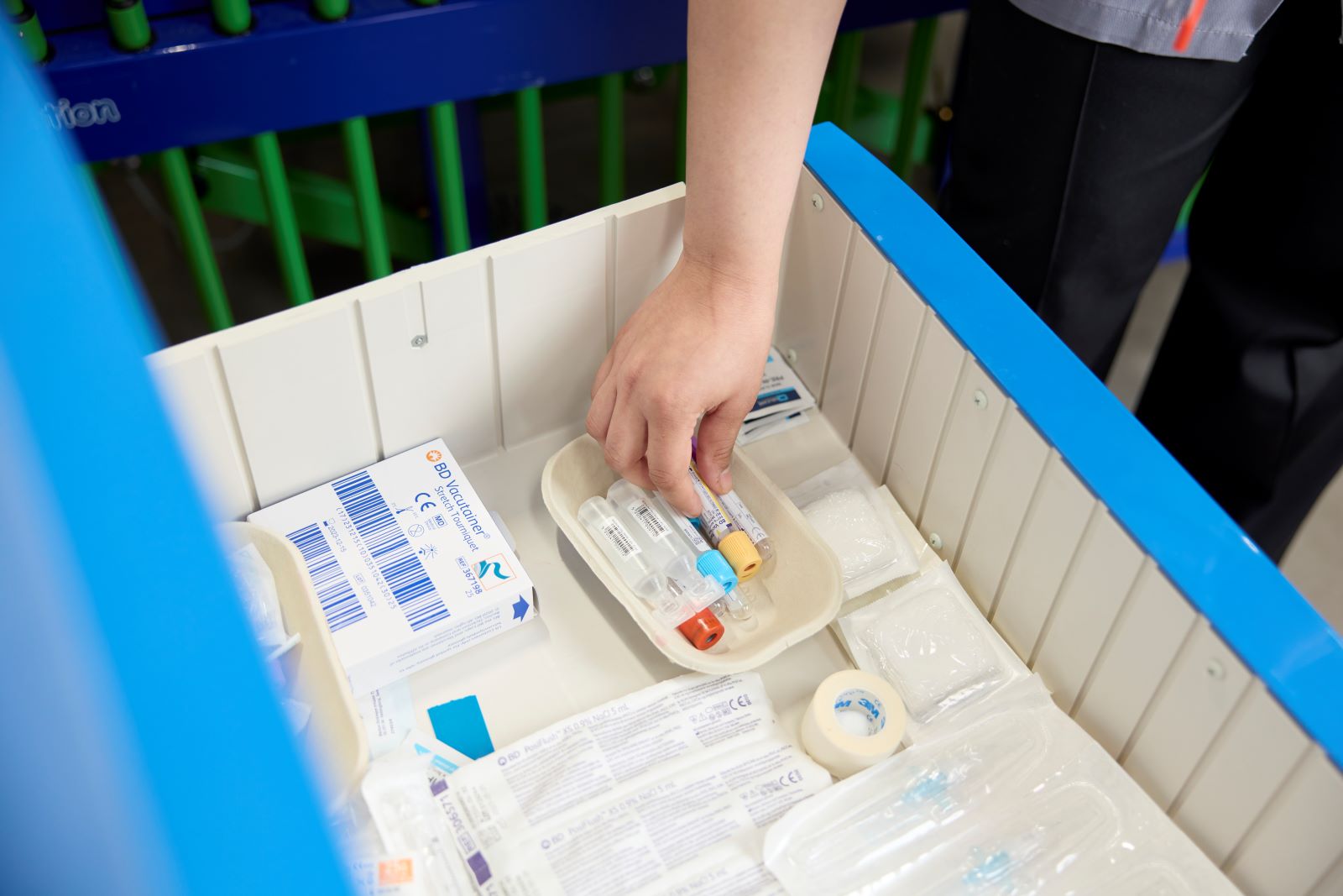 A student nurse selects a blood collection tube from a selection of medical supplies in a drawer.