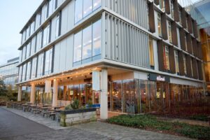 Outside view of Waterside restaurant from path. There is an alfresco seated area with benches and chairs below a string of softly-lit bulbs.