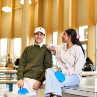 Image of two students leaning against a table tennis table in the Market.