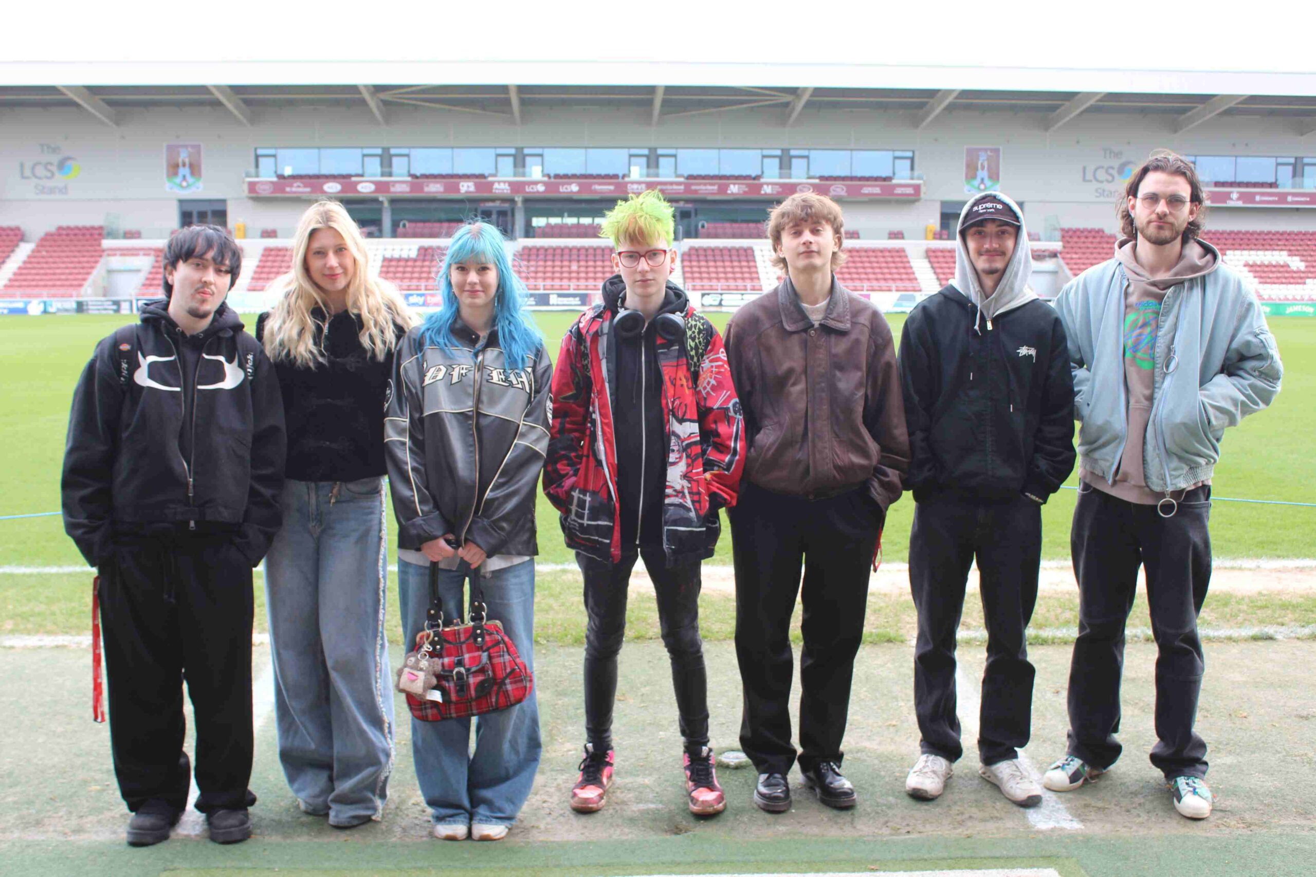 Group of seven students stand in front of football pitch.