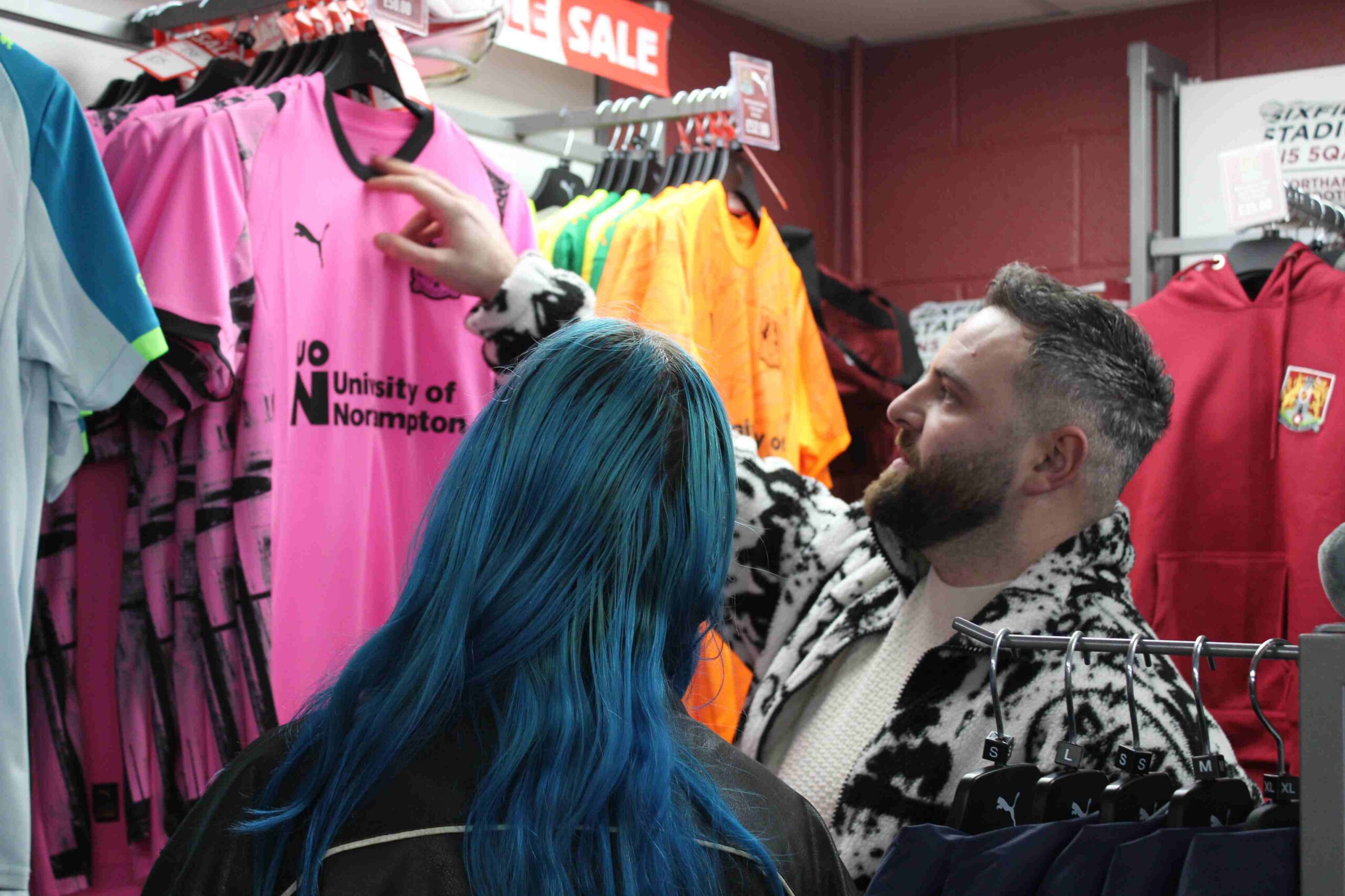 Two people look at shirts in NTFC shop.