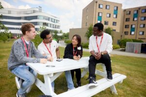 Four students sit on a white picnic bench at Waterside campus.