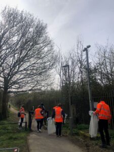 A group of people wearing orange high-vis jackets and vests collect litter on an outside path.