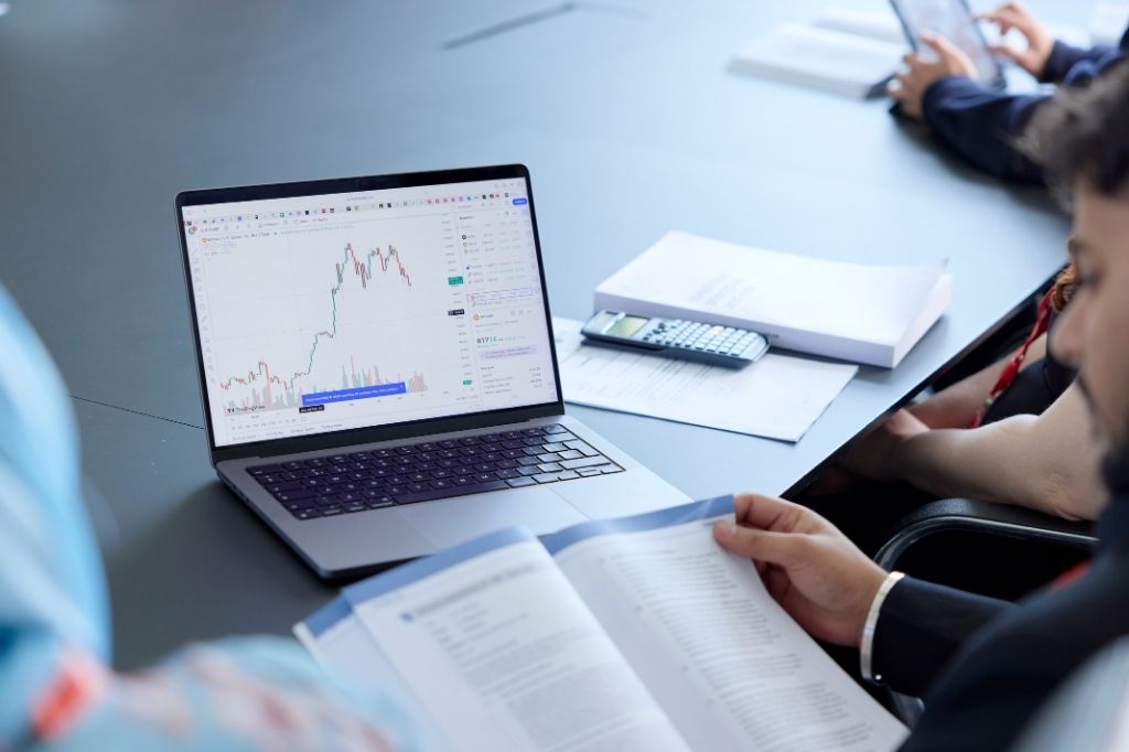 Laptop on a table with note books and finanicial data.