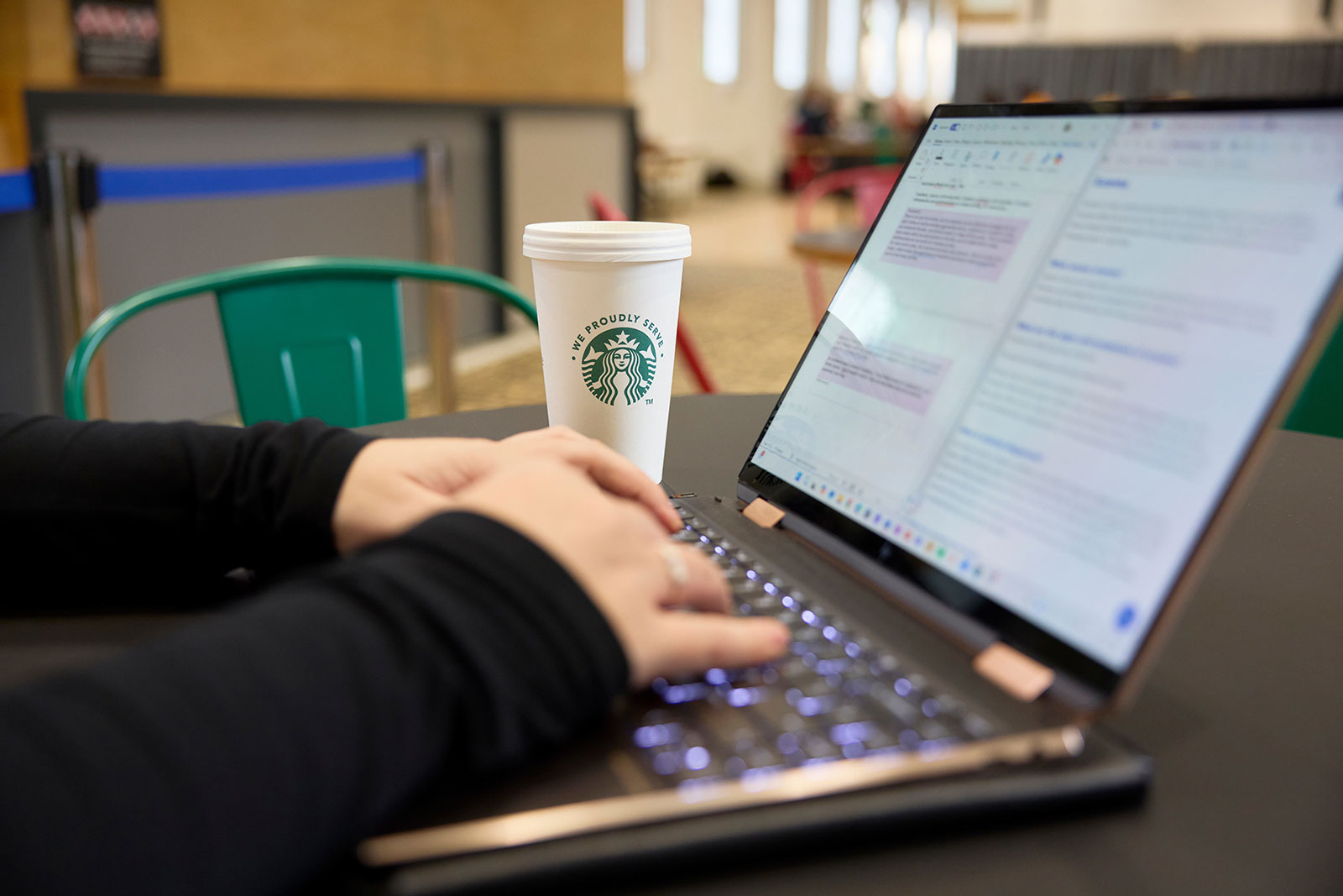 Image of a close up of student hands on a laptop with two documents open, a starbucks coffee cup next to their hands.