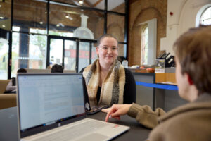 Photo of a student sitting opposite another student in the Engine Shed, both are on laptops.