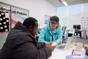 Picture of a student on their phone sitting next to a student futures staff member who has a laptop.