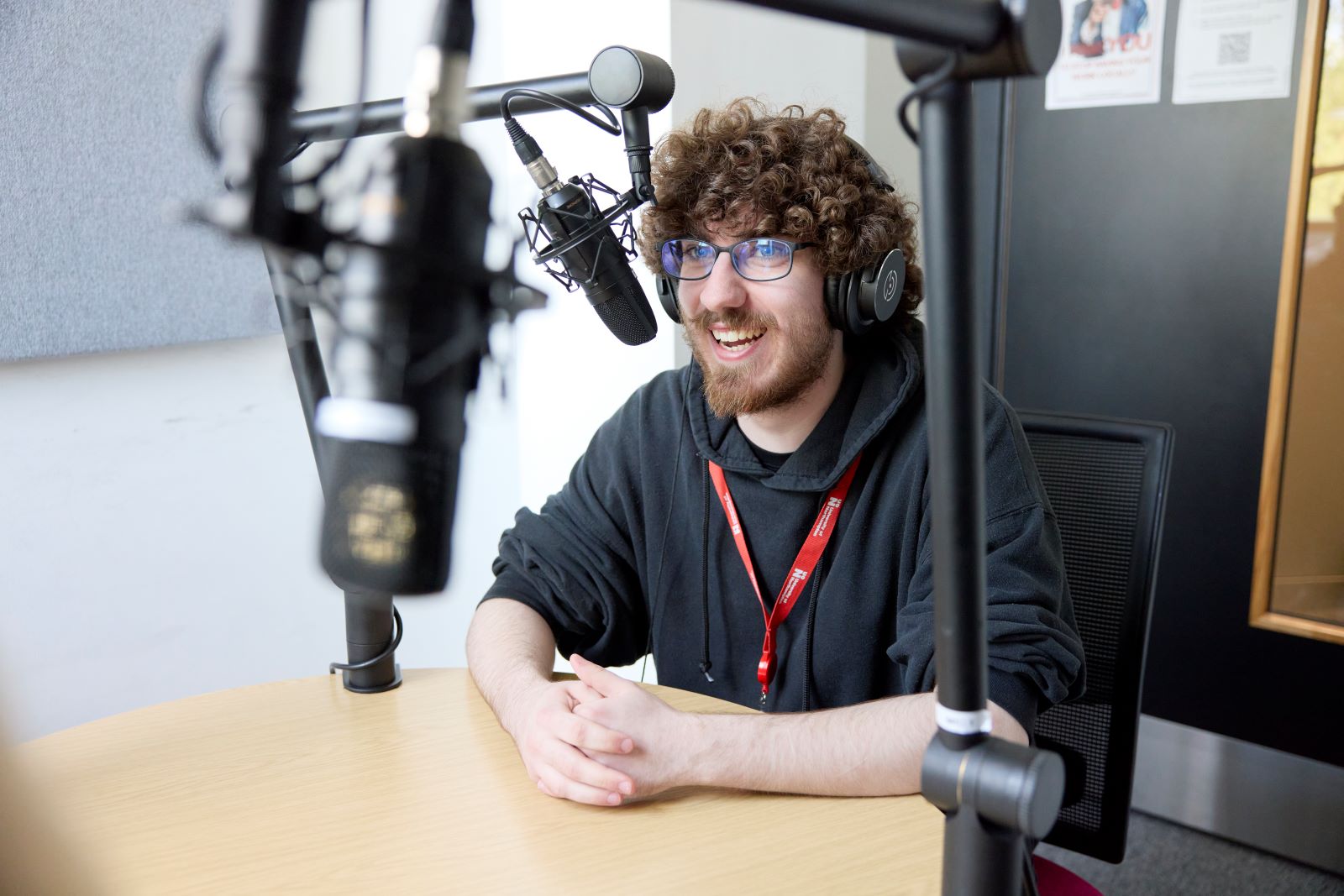 Student wearing glasses and a headset speaks into a podcast microphone.