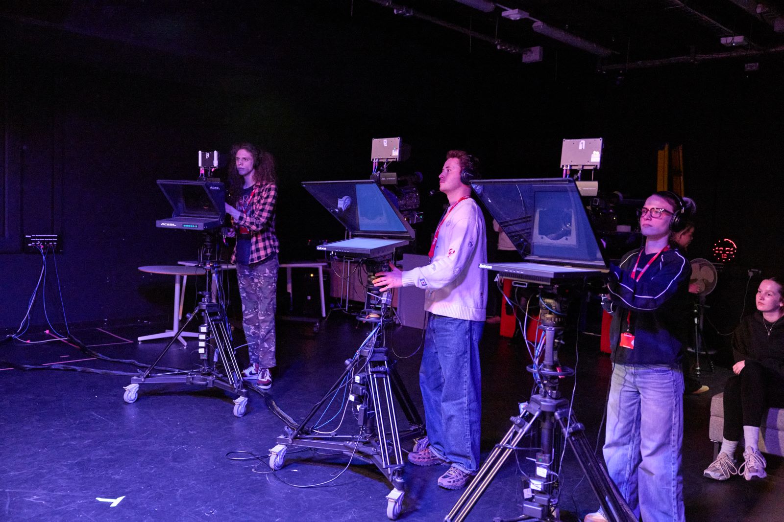 Three students using professional video cameras in a dimly-lit TV studio.