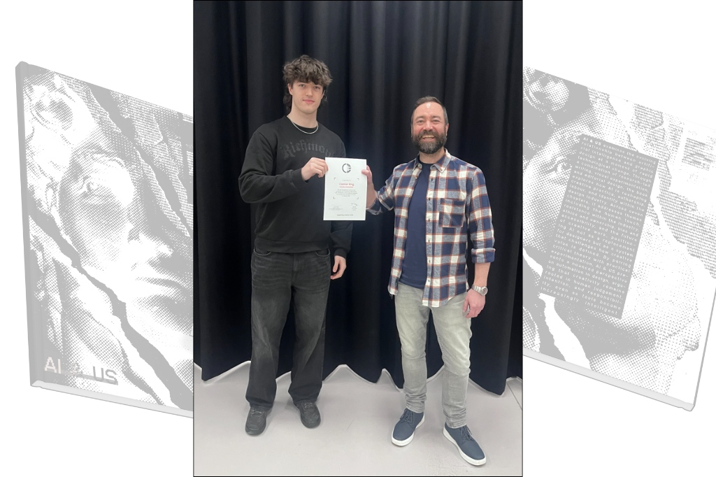 Connor stands next to another person and both are holding a certiifcate and smiling at the camera.