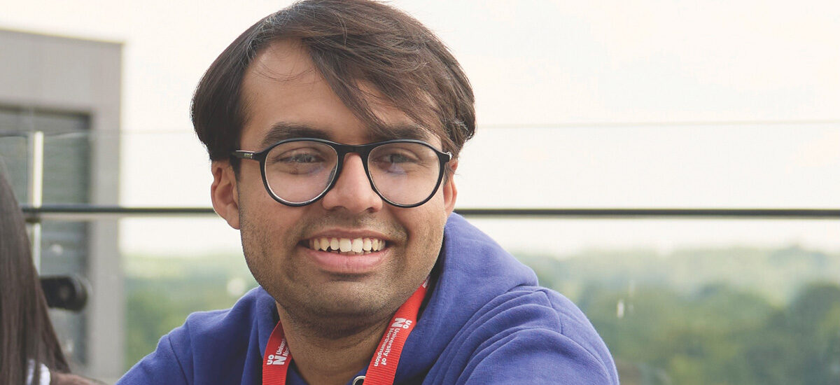 Close-up of Ishmam Yaseen Taha, an International Business Management BA (Hons) student, sitting at the balcony the sky and trees behind.