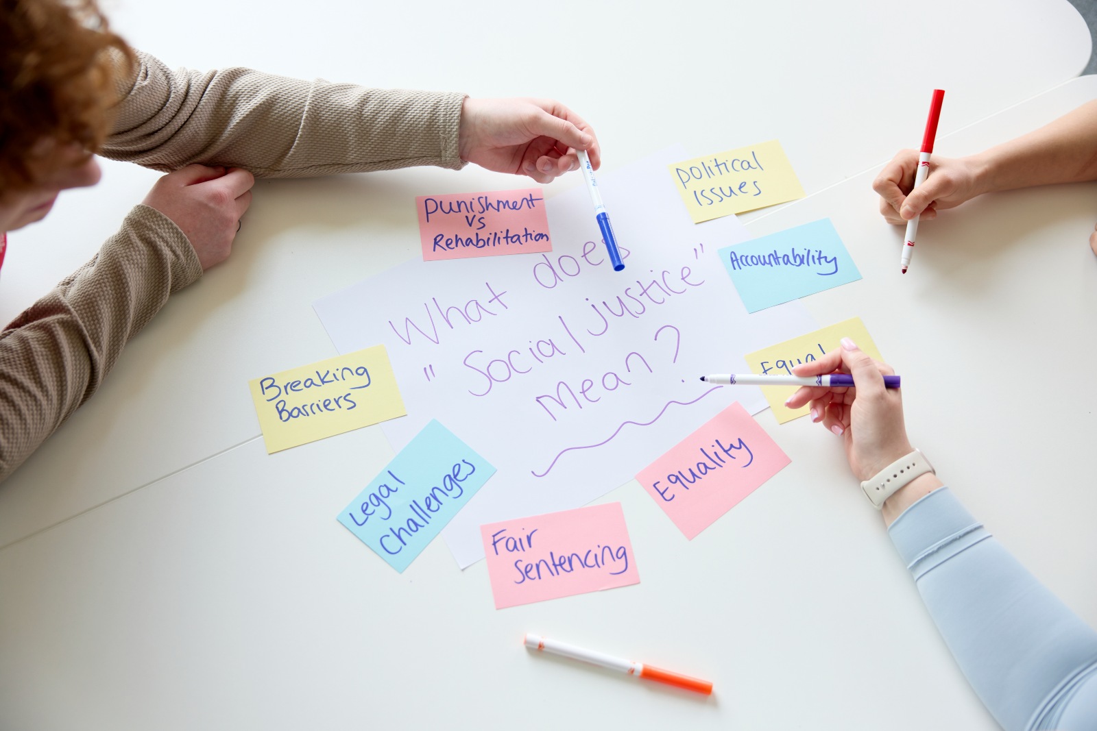 Students collaborating around a table using sticky notes and handwritten ideas during a seminar on social justice.