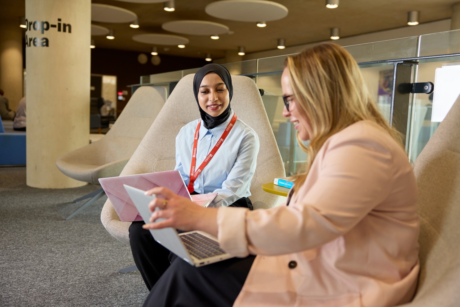 Student and member of university staff sitting together, reviewing work on laptops.