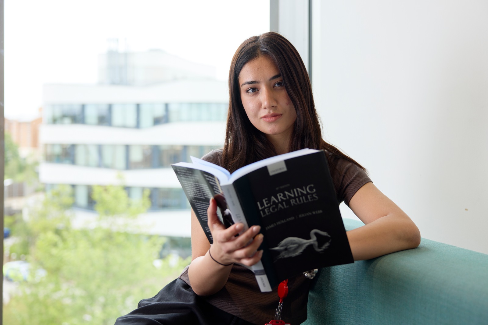 Student reading a law textbook while sitting by a large window on the University of Northampton campus.