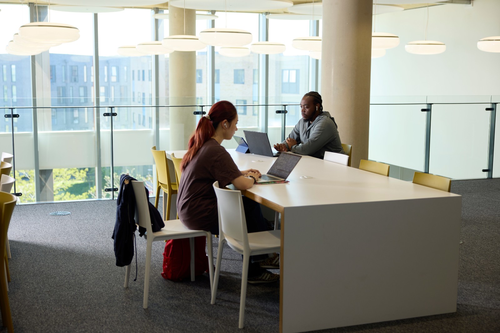 Two students on their laptops sat at a desk inside the learning hub study area