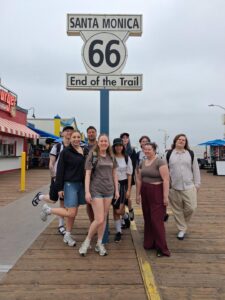 A group of nine Geography and Environmental Science students stand by a Route 66 sign on an overcast day. The group are casually dressed in trainers, and many are wearing rucksacks.