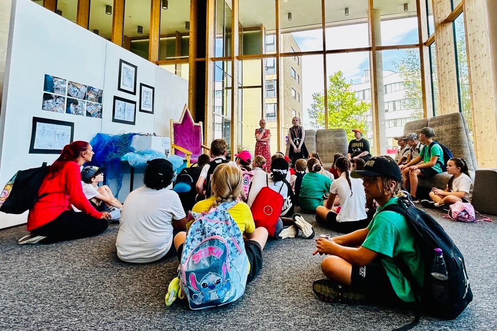 Primary school children sat on the floor of a high ceilinged, glass walled exhibition space as Children of Rectory Farm School see their work displayed at the Take One Picture Exhibition at University of Northampton.